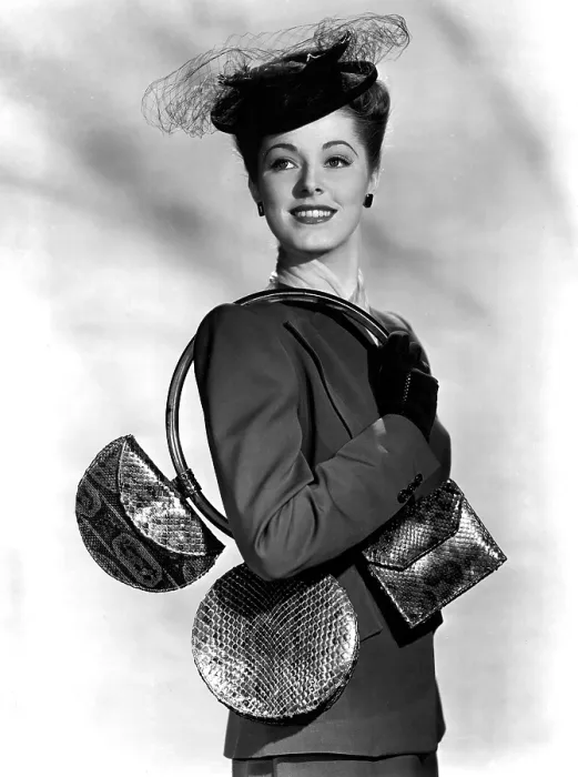 Framed Print : ELEANOR PARKER carrying 3 small handbags of blueberry red reptile and an over the shoulder hoop of plastic. 1945