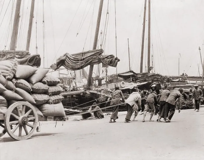 Framed Print : Gang of five Chinese dock workers lean hard on ropes to haul a heavy wagon load of sacks on the Hong Kong waterfront. Between 1890 and 1923