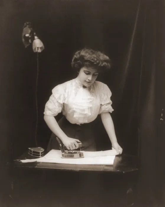 Framed Print : General Electric advertising photo of a woman using an electric iron plugged into light socket, ca. 1908
