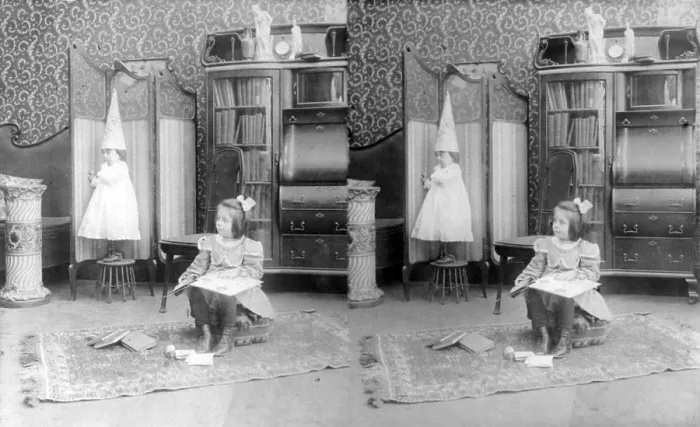 Framed Print : Girl seated in middle of room with books, smaller child standing on stool and wearing dunce cap, stereo photograph, circa 1908 Framed Print : Girl seated in middle of room with books, smaller child standing on stool and wearing dunce cap, stereo photograph, circa 1908