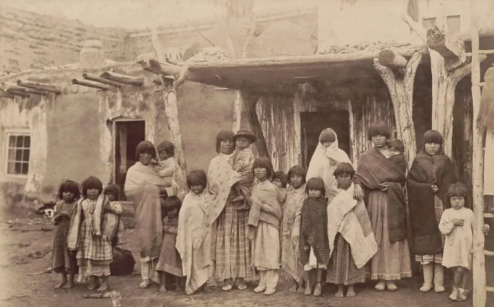 Framed Print : A group portrait photograph of nineteen women and children at Tesuqua Pueblo, ca. 1890-1900. The post and beam supports of the Pueblo architecture are evident