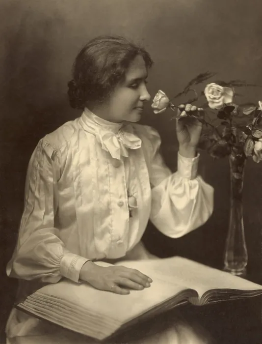 Framed Print : Helen Keller seated with her hand on braille book as she smells a rose in a vase, 1904
