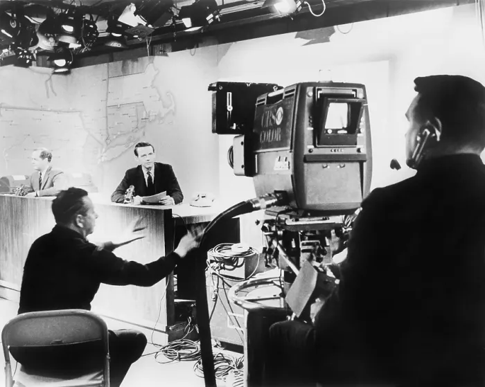 Framed Print : Under hot studio lights, a CBS News anchor performs under the director of his producer (seated between anchor and camera), for a color television camera in 1967 Framed Print : Under hot studio lights, a CBS News anchor performs under the director of his producer (seated between anchor and camera), for a color television camera in 1967