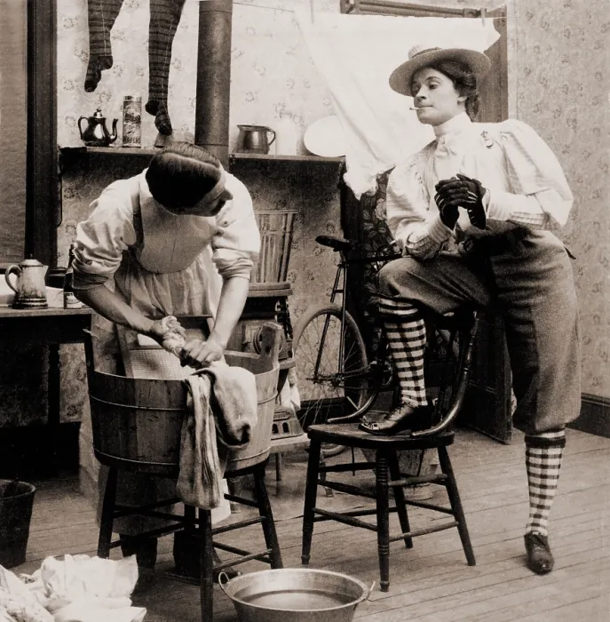 Framed Print : Humorous scene of life with the new woman. Woman smoking and wearing knickers postures arrogantly as a man drudges over laundry. 1901
