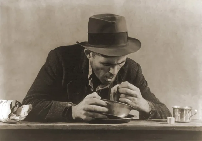 Framed Print : Hungry man with his meal of bread and soup at a New York City soup kitchen during the Great Depression. His fedora and now ragged sports jacket indicate his past employment. 1930s