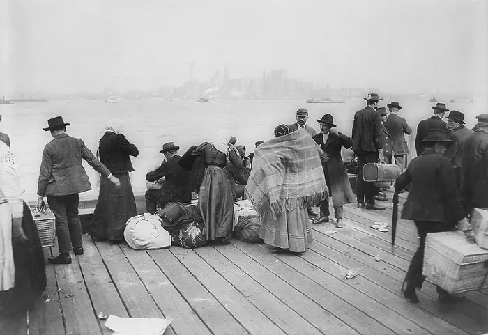 Framed Print : Immigrants waiting to be transferred by Ferry from Ellis Island, on October 30, 1912. In the background is the skyline of downtown Manhattan