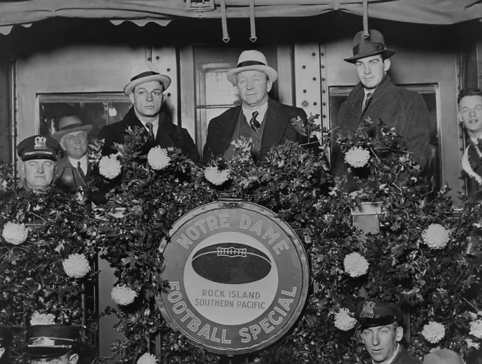 Framed Print : Knute Rockne standing on rear of train car decorated with flowers, 1930. Rockne is flanked by Coach Frank Cariedo and football player Tom Conley as they leave for California