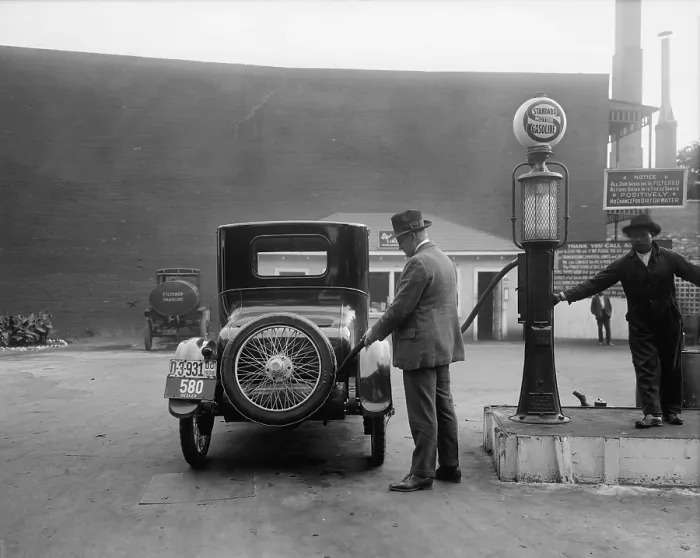 Framed Print : Man fueling his car at a self-service Standard Motor gas station in Washington D.C. area. A sign tells customers the gasoline is filter and contains no dirt or water. 1920