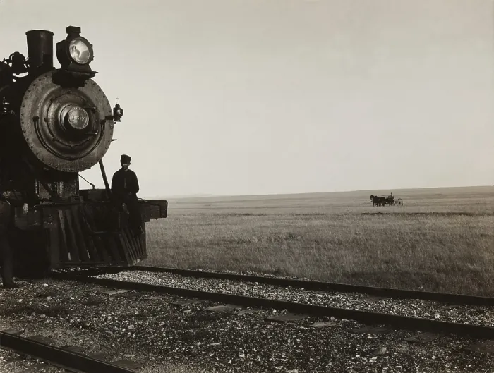 Framed Print : Two men standing on the cow-catcher of a Great Northern Railroad locomotive on the Montana prairie. In the grassy background is a horse-drawn carriage. Ca. 1910