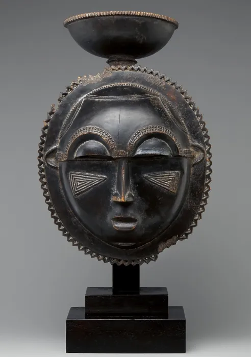 Framed Print : MOON MASK, 1880s, Baule peoples, Ivory Coast, Africa, sculpture, wood. Round wooden mask has a oval face edged by a zigzag border and topped with a cup