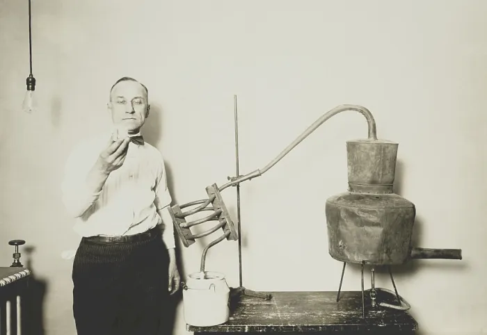 Framed Print : Moonshine still recently confiscated by the Internal Revenue Bureau. An employee holds a glass of alcohol distilled from the apparatus at the Treasury Department, ca. 1921-32