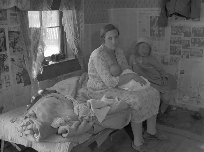Framed Print : Mother nursing her infant on a bed with another young child, surrounded by the news papered walls of a shack in the Missouri Ozarks. Photo by Carl Mydans, June 1936