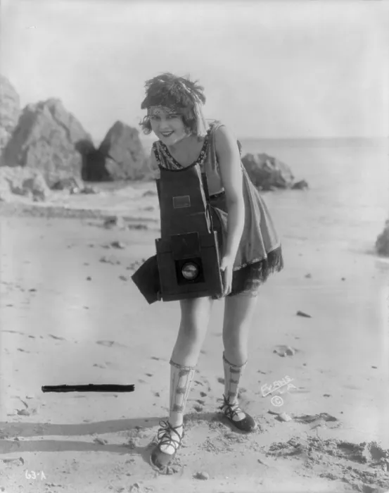 Framed Print : Myrtle Lind, a young woman posing with a Graflex camera on a beach, 1919