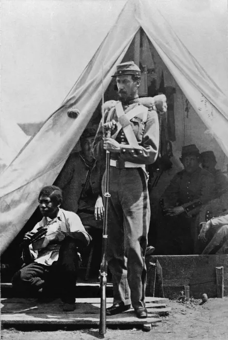 Framed Print : A New York State soldier poses before his tent at Camp Cameron holding his bayoneted rifle with an African American contraband boy shining shoes at his side