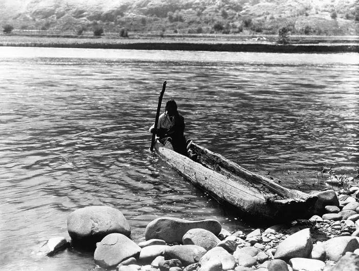 Framed Print : Nez Perc canoe. Nez Perc man with pole maneuvering dugout canoe to rocky shore. Edward S. Curtis, ca. 1910