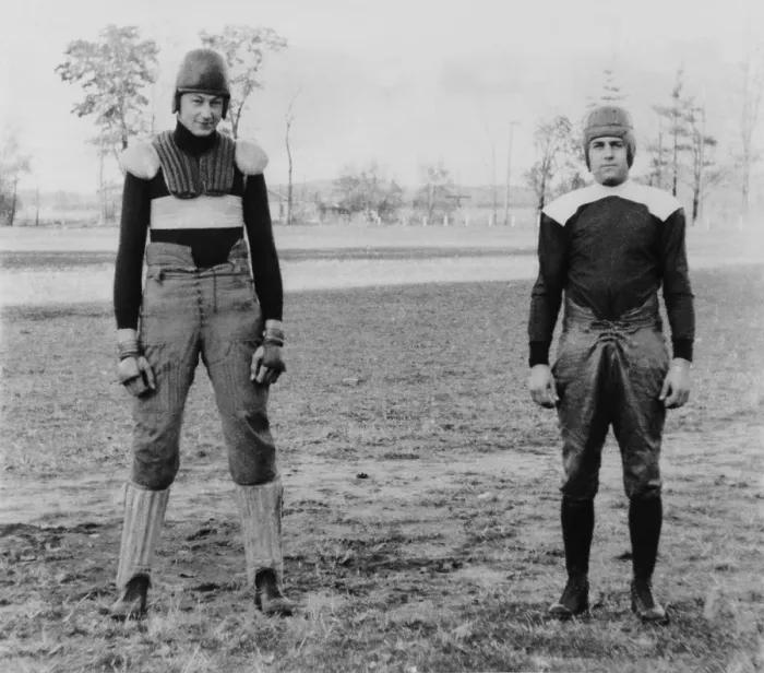 Framed Print : Notre Dame University football players wearing old and new football uniforms. At left is a football suit of the 1880's with external padding
