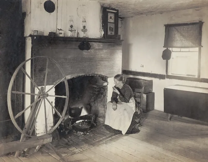 Framed Print : OLDEN TIMES. Middle aged woman watching her cooking from a rocking chair by a fireplace as she smokes a pipe
