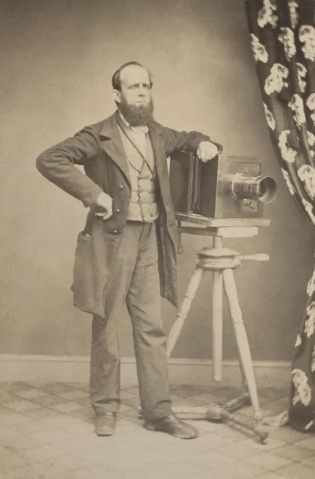 Framed Print : Photographers full length portrait standing next to a box camera resting on a tripod in a photo studio, c. 1866-75. It is possibly of a portrait of Charles L
