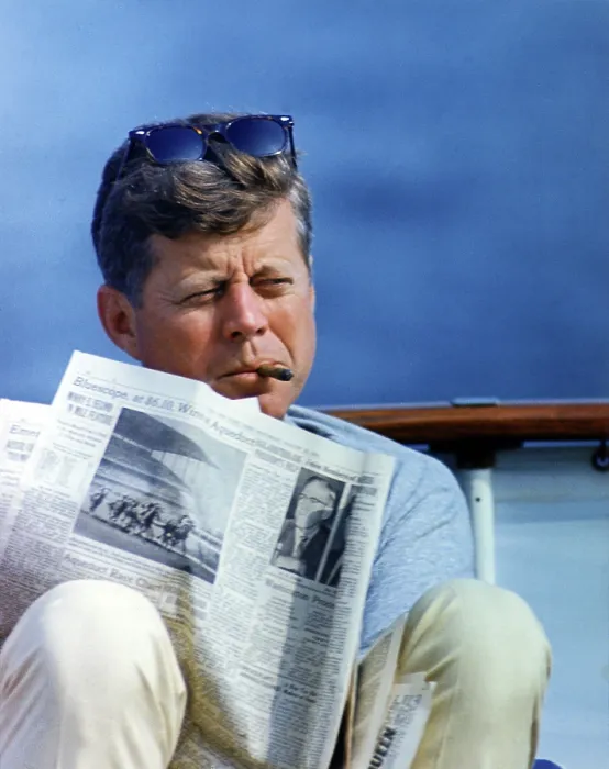 Framed Print : President John Kennedy smoking a cigar while reading the New York Times, aboard the family yacht, Honey Fitz in Hyannisport, Massachusetts. 1963