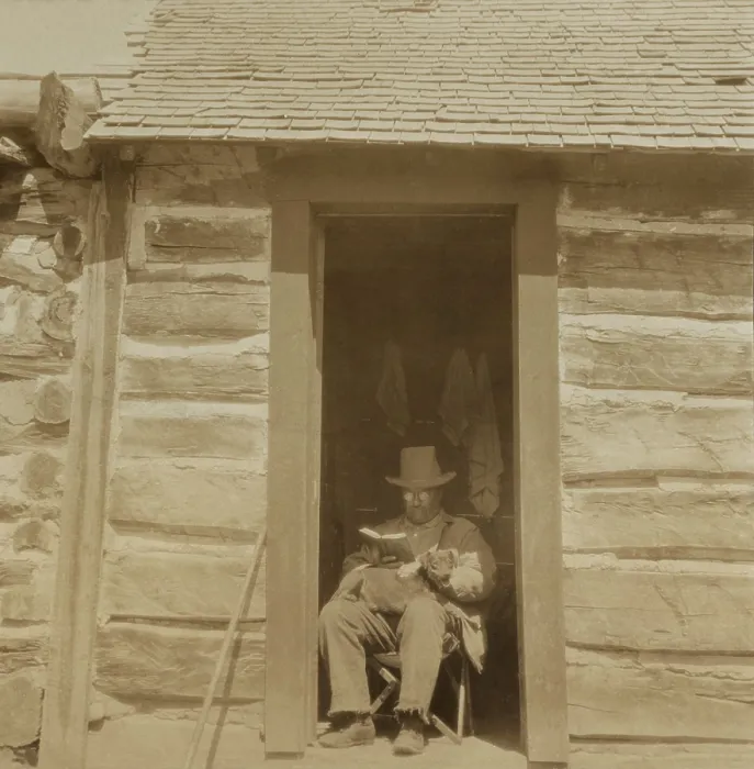Framed Print : President Theodore Roosevelt reading in the doorway of West Divide Creek Ranch House. In his lap is the hunting dog Skip he adopted and took back to Washington