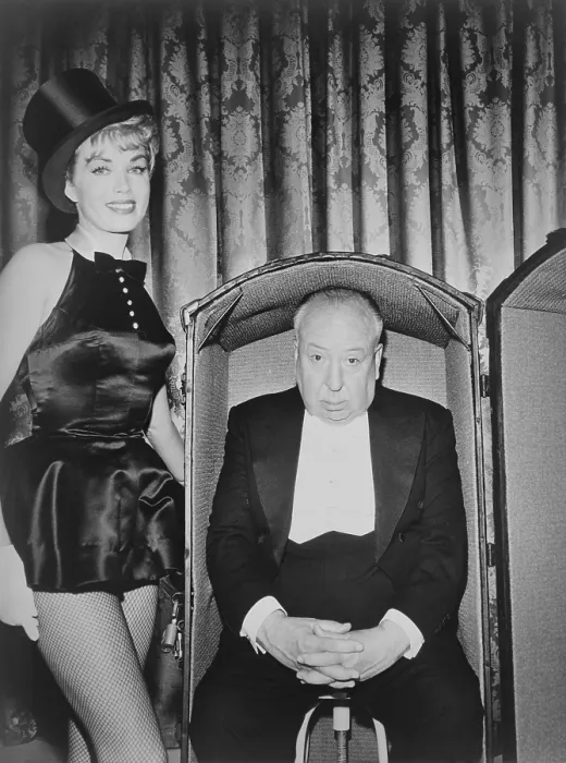 Framed Print : Producer Alfred Hitchcock seated inside a trunk, grimly awaiting the actions of actress Kim Novak, costumed as a magician's assistant. Publicity photo, Sept