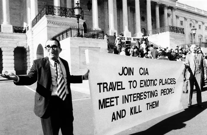 Framed Print : Rally protesting U.S. involvement in Angola. Demonstrators in front of the Capitol wear masks of Henry Kissinger and a pig. Their sign reads, Join CIA