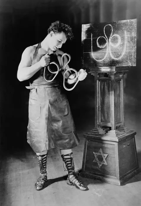 Framed Print : Sigmund Zishe Breitbar, in his blacksmith costume as he bends an iron bar into a trefoil. Ca. 1924