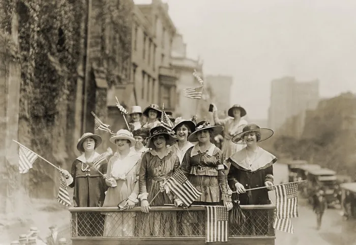 Framed Print : Smiling young women waving flags from the top of an open vehicle in a New York City parade. Ca. 1910-1915