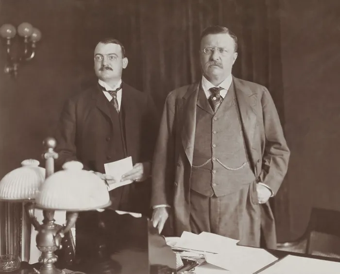 Framed Print : Theodore Roosevelt standing behind desk, with Asst. Presidential Secretary William Loeb, 1902. At that time, George B