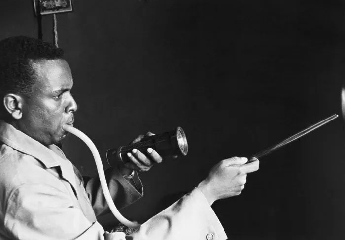 Framed Print : Togolese man using a mouth inhaler to capture mosquitoes to prevent the spread of malaria. 1964