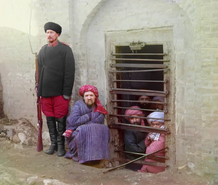 Framed Print : Traditional Central Asian prison, with cells cut into the ground. Turbaned Inmates looking out through the bars while guard stands by with a Russian rifle, uniform, and boots Framed Print : Traditional Central Asian prison, with cells cut into the ground. Turbaned Inmates looking out through the bars while guard stands by with a Russian rifle, uniform, and boots