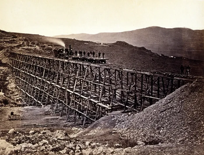 Framed Print : Trestle work. Central Pacific Railroad construction workers standing on railroad flatcars being pushed by locomotive across trestle at Promontory Point in Salt Lake Valley