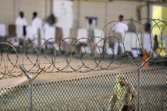 Framed Print : A U.S. Sailor foreground conducts an early morning patrol while detainees dressed in white background at a recreation yard inside Camp Delta at Guantanamo Bay Naval Base Cuba Framed Print : A U.S. Sailor foreground conducts an early morning patrol while detainees dressed in white background at a recreation yard inside Camp Delta at Guantanamo Bay Naval Base Cuba