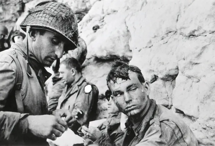 Framed Print : U.S. soldier who was injured during landing on Normandy beachhead, on D-Day plus 1. A medic bandages his hand. The marks on his face came from water spray while landing