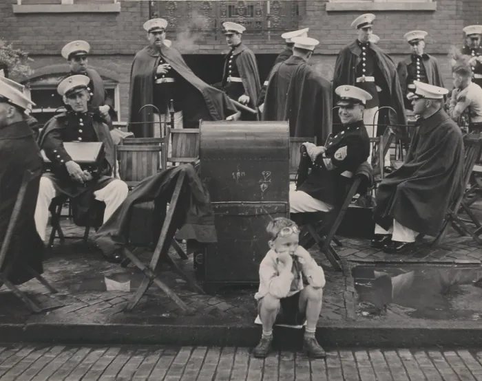Framed Print : Watching for the parade, child seated on a curb with a military band behind, photograph by Louise Rosskam, North Street, Washington DC, 1938