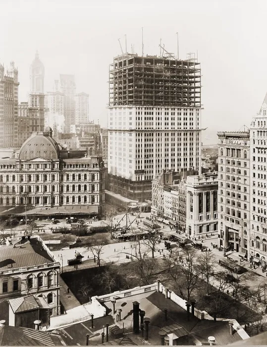 Framed Print : Woolworth Building, partially-constructed building amidst smaller buildings. The lower floors have received a white terra-cotta facing worked in lacy Gothic style
