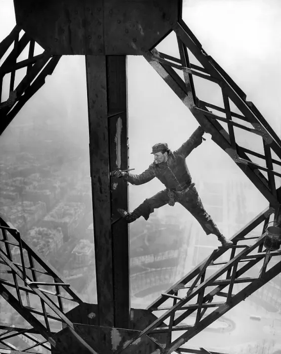 Framed Print : Worker painting the Eiffel Tower. Working without a safety harness he precariously straddles steel beams