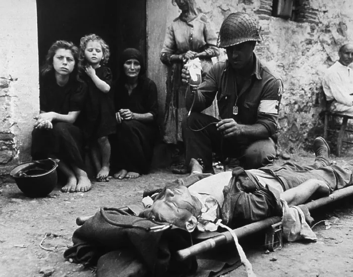 Framed Print : Wounded U.S. soldier receives blood plasma while lying on a stretcher in a street in Sicily during World War II. Behind the medic, barefoot Sicilian civilians watch. 1943 Framed Print : Wounded U.S. soldier receives blood plasma while lying on a stretcher in a street in Sicily during World War II. Behind the medic, barefoot Sicilian civilians watch. 1943