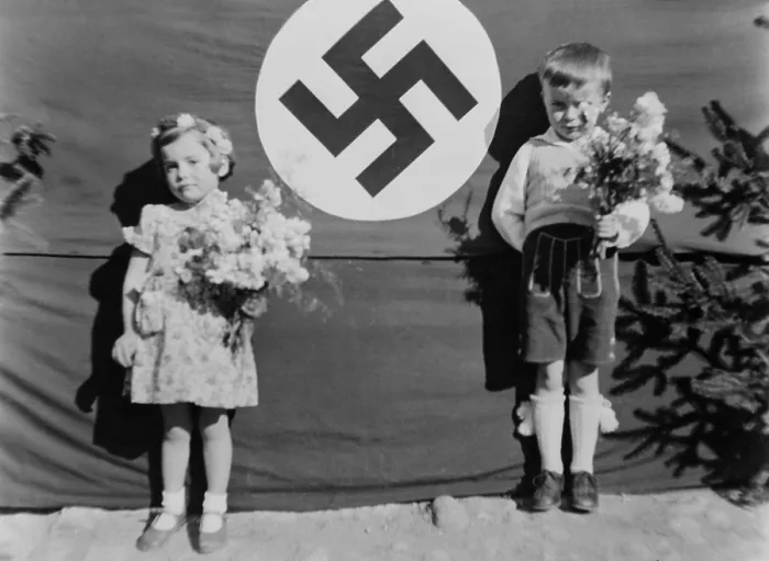 Framed Print : Young German girl and boy at a Nazi ceremony, ca. 1937. They hold flowers and stand beside a large swastika, in Muhldorf am Inn, Germany. (BSLOC_2013_11_28) Framed Print : Young German girl and boy at a Nazi ceremony, ca. 1937. They hold flowers and stand beside a large swastika, in Muhldorf am Inn, Germany. (BSLOC_2013_11_28)