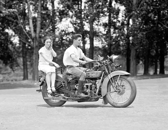 Framed Print : A young man drives a motorcycle while a young woman rides side saddle behind him. ca. 1929-1930
