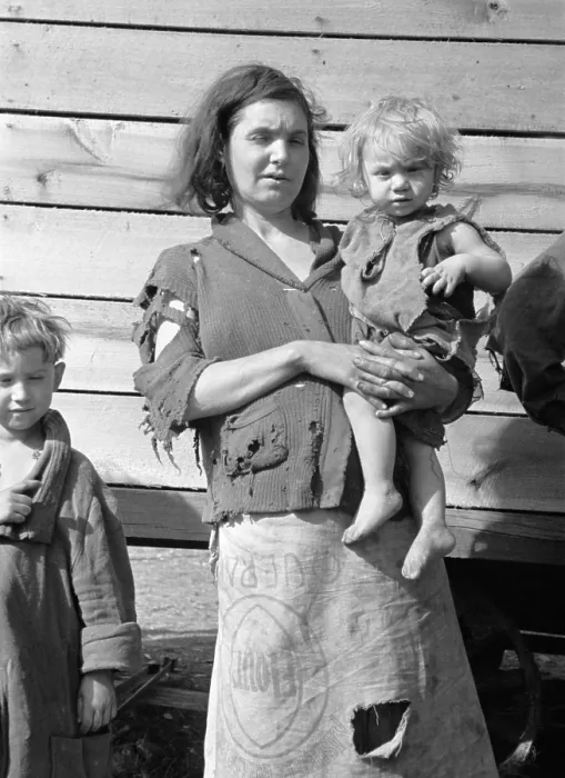 Framed Print : Young mother dressed in a ragged sweater and a skirt made of flour sacks holds her toddler. She lives with eight others in a field on U.S
