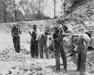 African American convicts in a Southern work gang breaking up rocks with sledge hammers. Ca. 1940