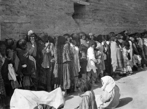Lined Up Prints: American Indians, Apache men, women and children outside agnecy building on issue day