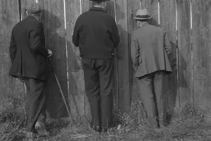 West Virginia Prints: The backs of three men watching a football game through cracks in a fence