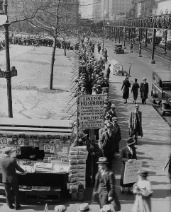 Breadline along Bryant Park in Mid-town Manhattan. A sign advertised meals for 1 cent and requests donations. New York City. 1930s