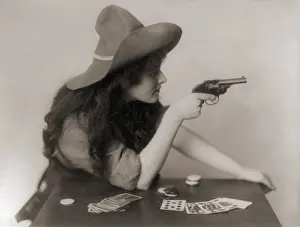 Revolvers Prints: Cowgirl with deck of cards and chips, pointing a pistol. 1912