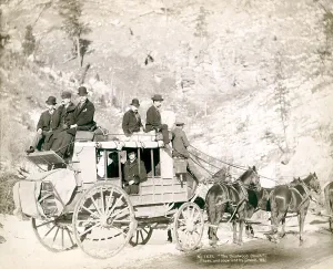 Stagecoach Prints: The Deadwood Coach. Side view of a stagecoach; formally dressed men sitting in and on top of coach