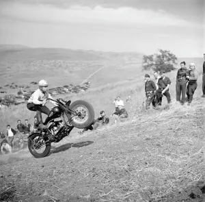 Rider Prints: An early motorcycle club watches as a member pops a wheelie on an uphill climb