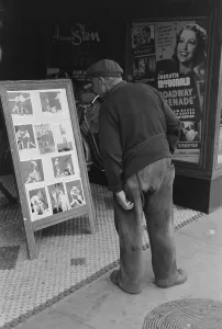 Russell Lee Photo Prints: Elderly man with patches clothing looking at stills of Joe Lewis fight