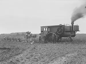 Machinery Prints: Three farmers stand by a huge steam tractor attached to six combined